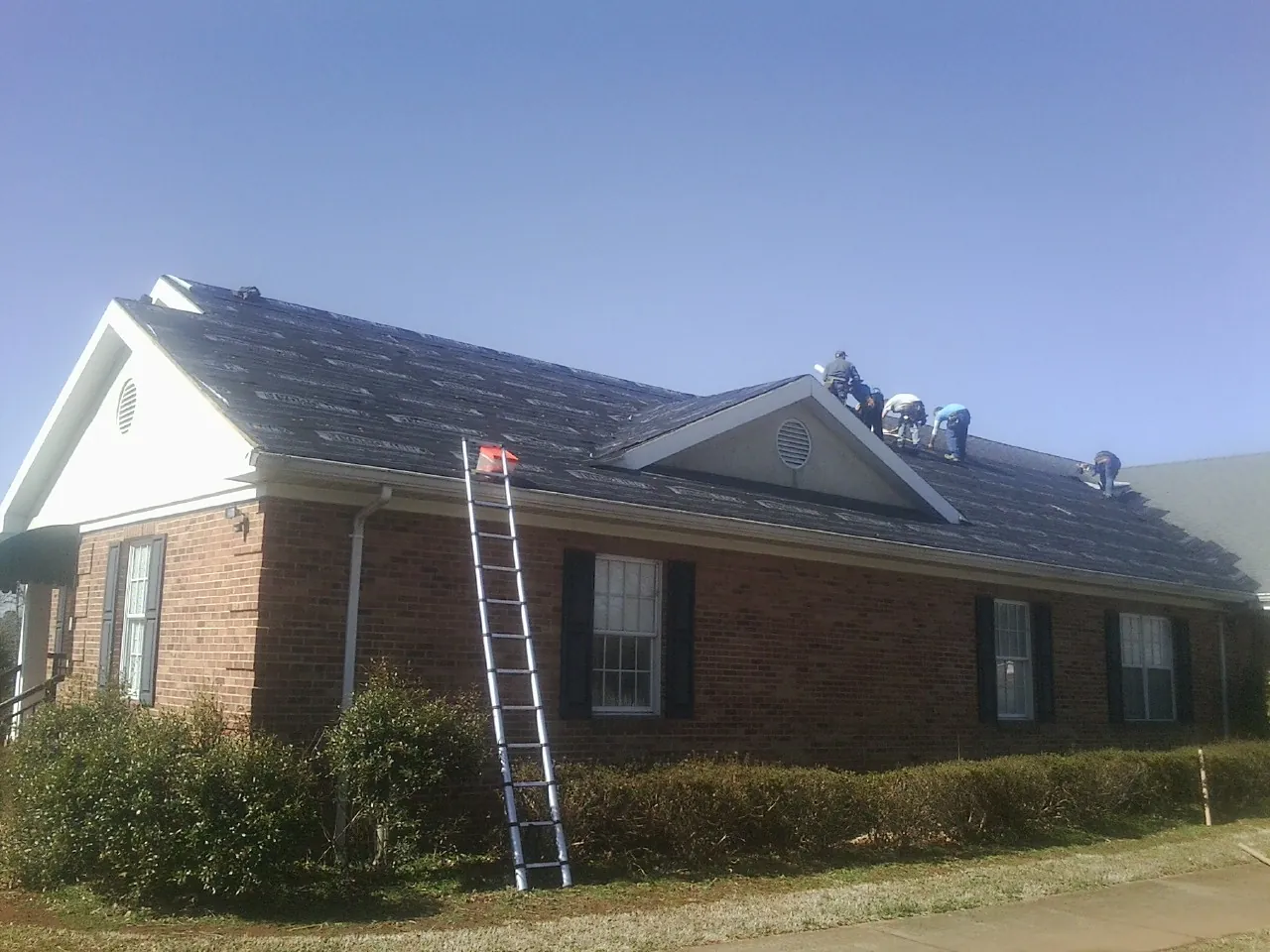 Crew tearing shingles off a brick ranch roof with a ladder set — Emergency Roof Repair work by our crew in Woodbine