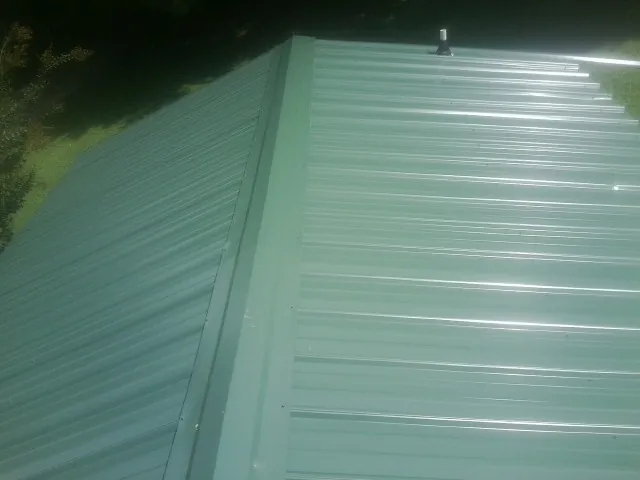 New green metal panels meeting at the ridge of a roof — Flat Roof Repair work by our crew in Woodbine
